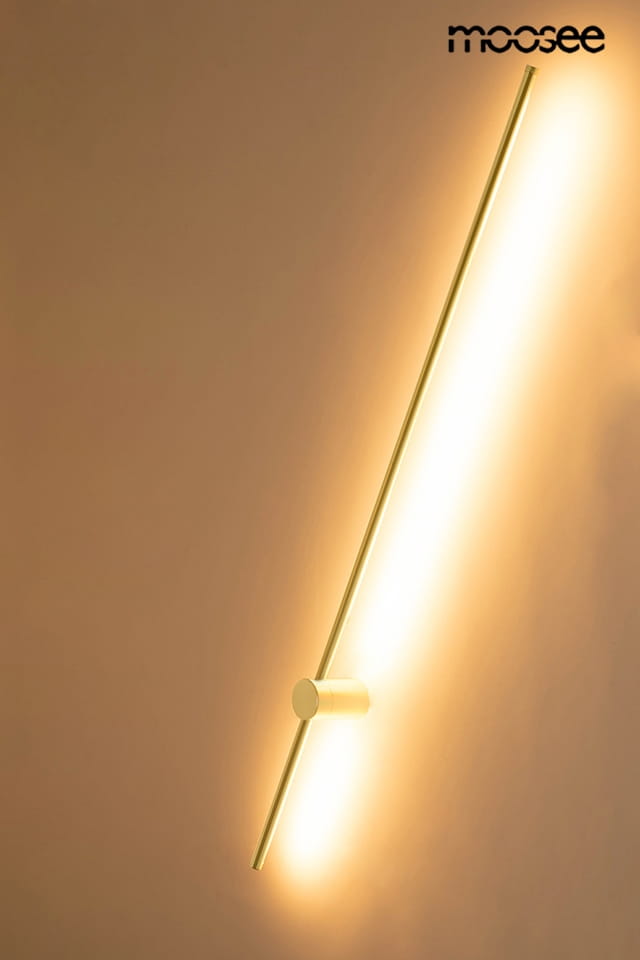 Kinkiet Ombre 120 w kolorze złotym, wykonany z metalu, z prostą, pionową konstrukcją. Zawiera jedną diodę LED o mocy 14W, emitującą ciepłe światło. Zainstalowany na ścianie, podkreśla nowoczesny styl wnętrza. Tło jasne, jednolite.