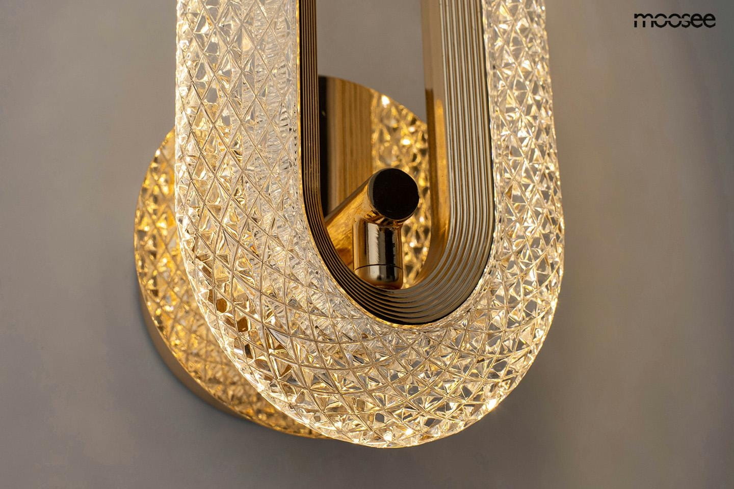 Kinkiet Jewel w kolorze złotym, z przezroczystym kloszem o diamentowej fakturze. Ujęcie z boku, ukazujące elegancki kształt oraz zamontowaną lampę LED 7W. Tło w stonowanym odcieniu, podkreślające produkt.