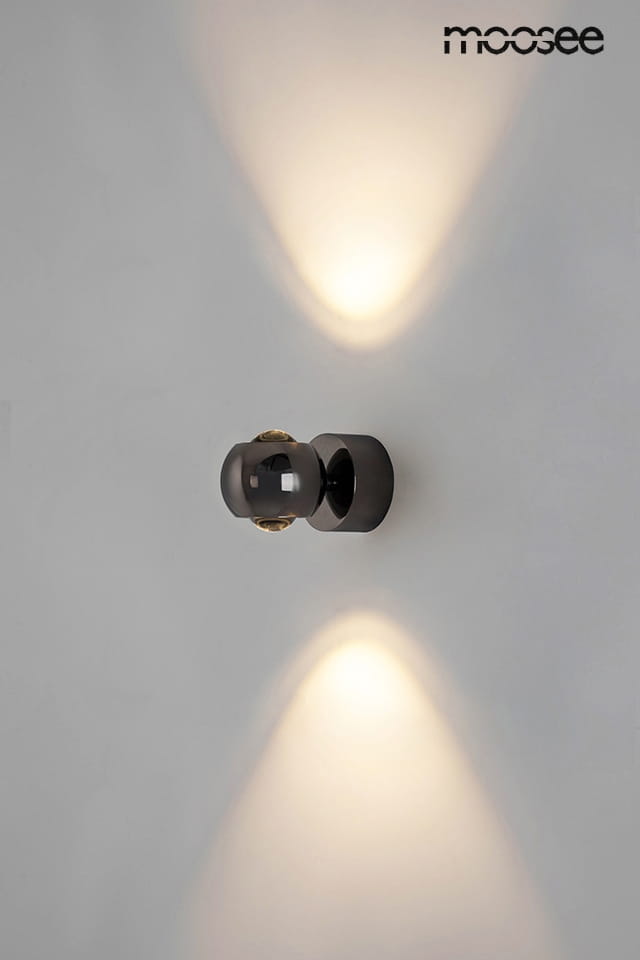 Kinkiet Eos 1xLED/8W w kolorze czarnym z chromowanymi akcentami. Ujęcie frontalne, montowany na ścianie. Zawiera okrągłą, przezroczystą kulę oraz emitującą światło w górę i w dół. Proste tło podkreśla elegancki design.