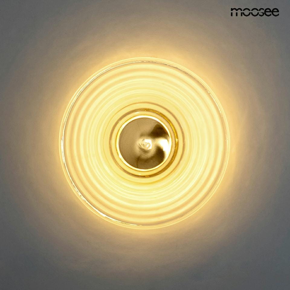 Kinkiet Onda LED 1xLED/9W w kolorze złotym, okrągły klosz z falistym wzorem, montowany na ścianie. Emituje ciepłe światło, centralny element w kolorze złotym. Tło jasne, minimalistyczne.