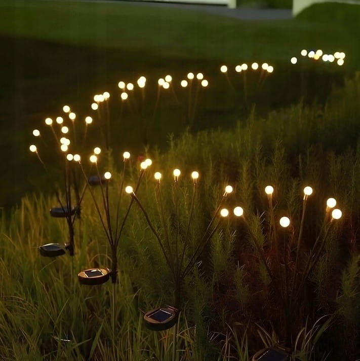 Lampa solarna ogrodowa z 6 diodami LED, czarna, umieszczona na szpikulcu. Widok z boku, z rozświetlonymi kulami umieszczonymi na cienkich, metalowych nóżkach. Lampa w trawie, tworząca dekoracyjny efekt świetlny w ogrodzie.