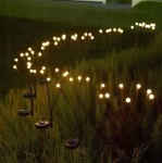 Lampa solarna ogrodowa z 6 diodami LED, czarna, umieszczona na szpikulcu. Widok z boku, z rozświetlonymi kulami umieszczonymi na cienkich, metalowych nóżkach. Lampa w trawie, tworząca dekoracyjny efekt świetlny w ogrodzie.