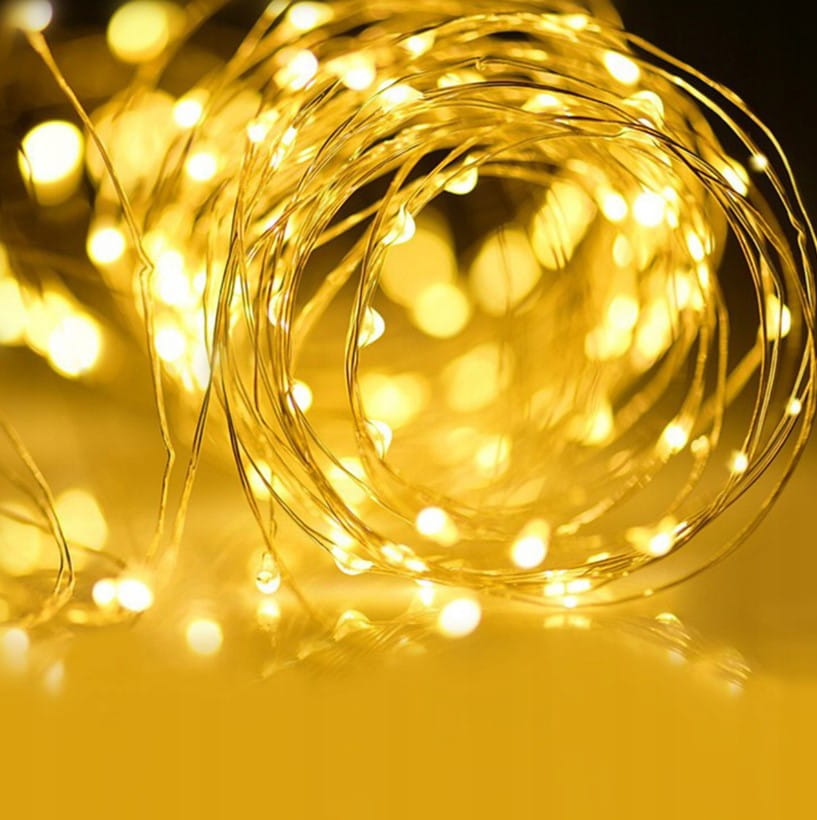 Girlanda świetlna ogrodowa solarna o długości 30 m z 300 diodami LED, w kolorze ciepłej żółci. Produkt zwinięty w kształt spirali, ukazuje delikatne, migoczące światło na ciemnym tle. Idealny do dekoracji ogrodów i przestrzeni na świeżym powietrzu.