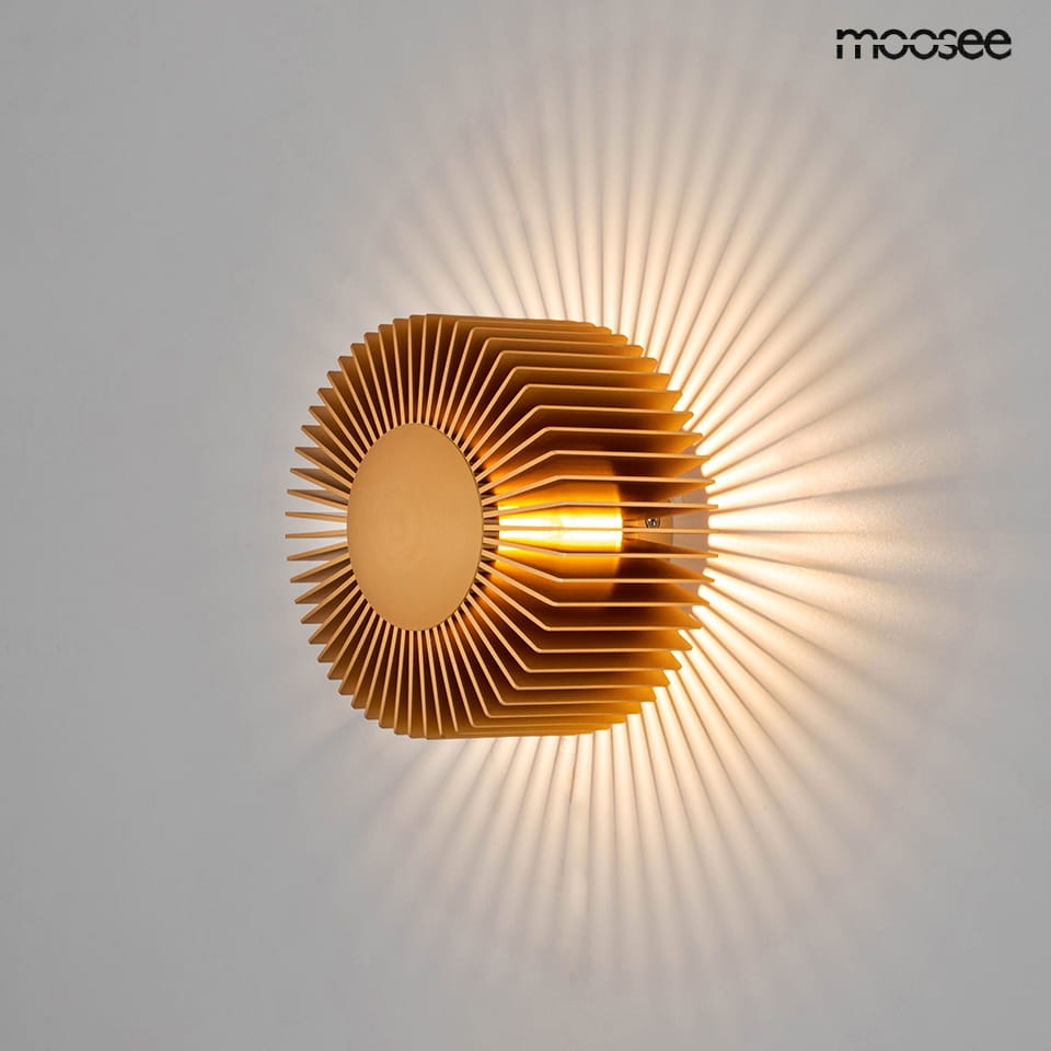 Złoty kinkiet Sunny z 1xLED/3W, o okrągłym kształcie z wyraźnie zaznaczonymi, falistymi żeberkami. Ujęcie frontalne, montowany na ścianie, z efektem świetlnym rzucającym promienie na ścianę. Prosta, elegancka forma.