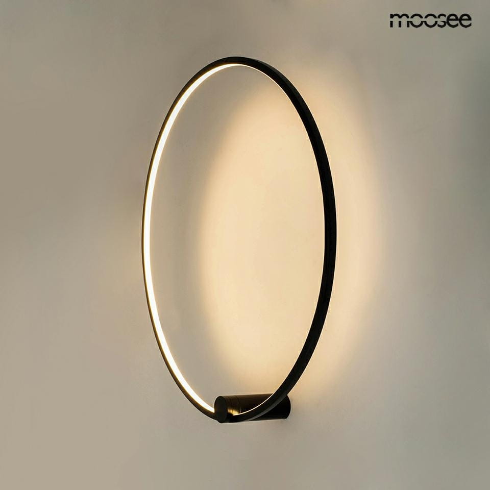 Kinkiet Hoop 60 w kolorze czarnym, o okrągłym kształcie, z zamontowanym źródłem światła LED o mocy 25W. Światło emituje delikatny blask wokół krawędzi, montowany na ścianie. Tło proste, jasne.