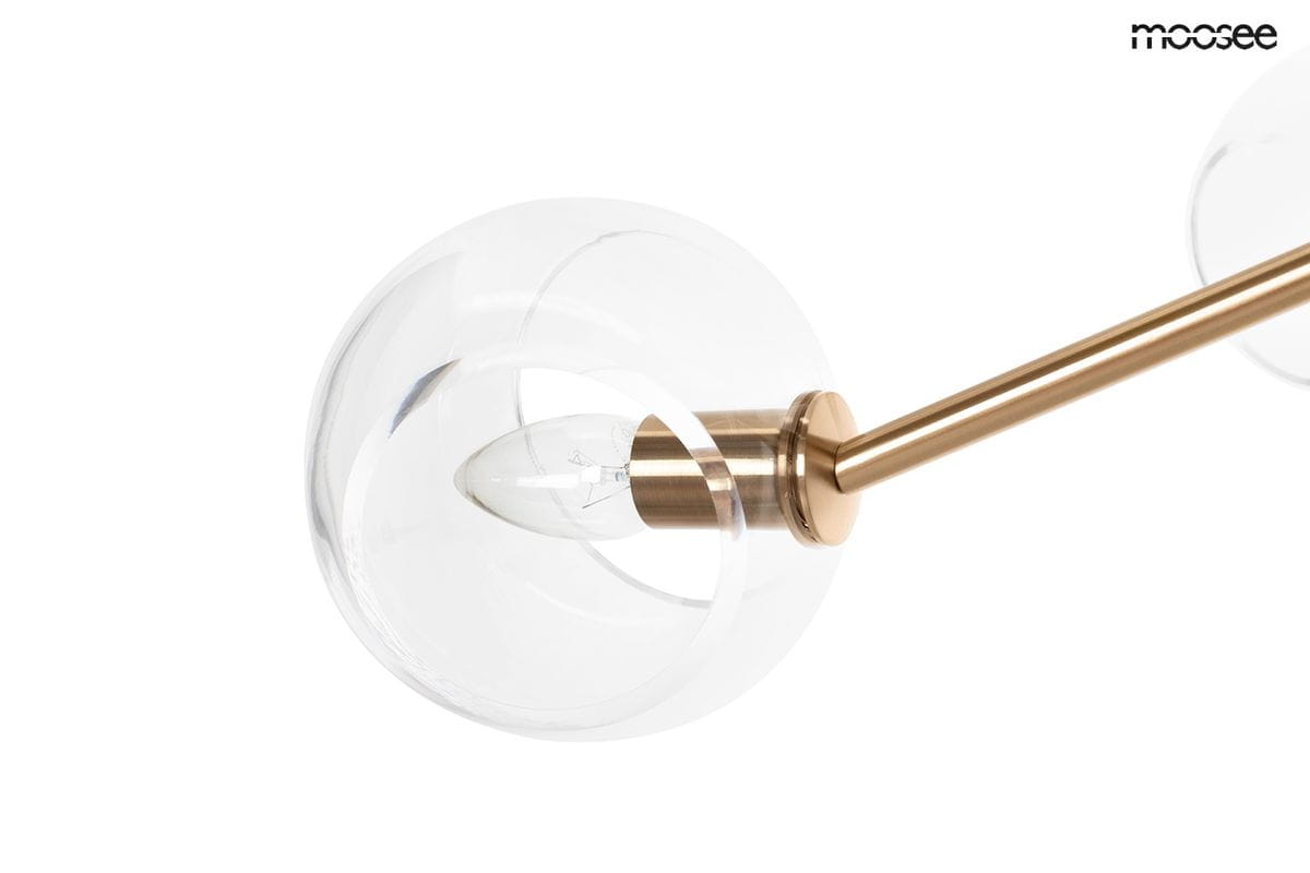 Lampa wisząca Aura z sześcioma miejscami na żarówki E14, z złotą metalową konstrukcją. Przezroczysta kula osłania źródło światła, podkreślając elegancki design. Ujęcie z boku, ukazujące detal mocowania i klosza.