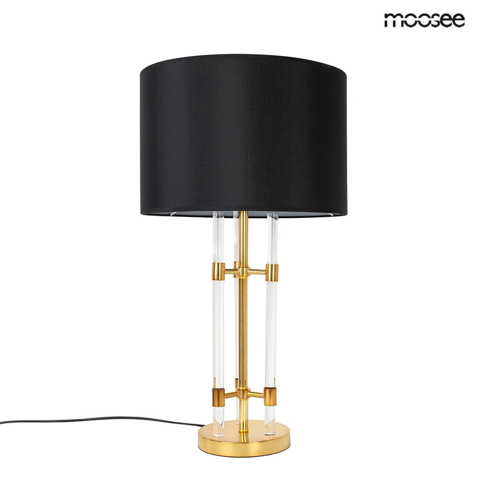 Lampa stołowa Moxy z podstawą w złotym kolorze i czarnym abażurem. Konstrukcja z przezroczystych elementów, stojąca z kablem zasilającym na dole. Abażur o klasycznym kształcie, podkreślający elegancki design.
