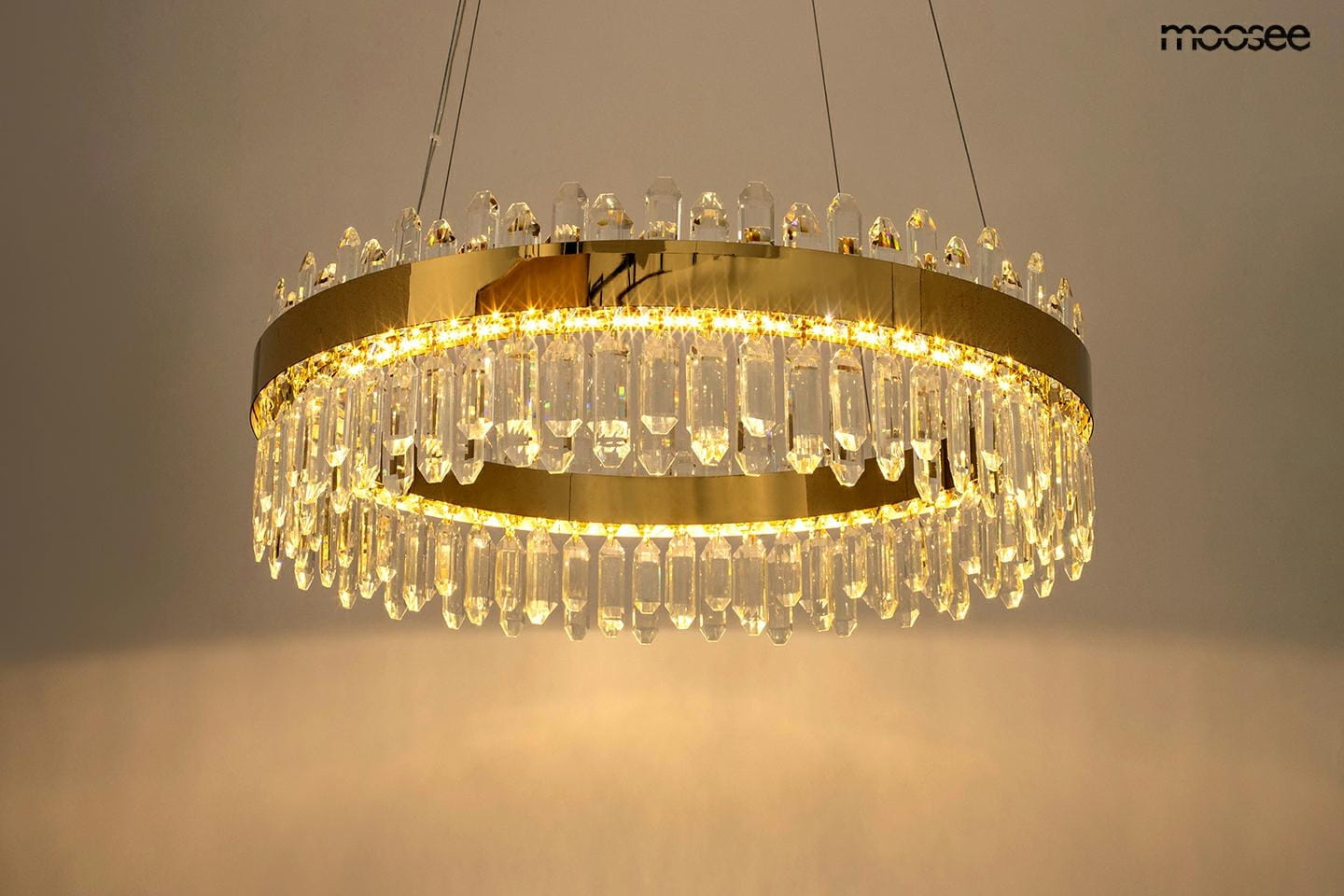 Lampa wisząca Amira 60 w kolorze złotym, z jednym źródłem światła LED o mocy 21W. Okrągła konstrukcja z przezroczystymi kryształami zawieszona na cienkich linkach, emitująca ciepłe światło.