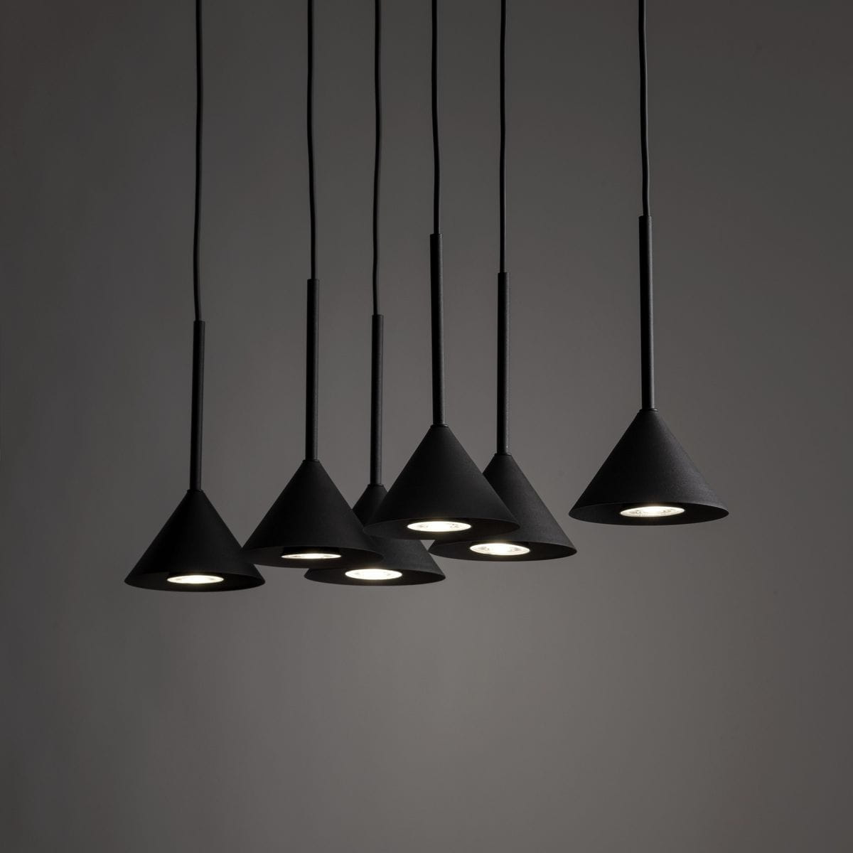 Lampa wisząca Cono z sześcioma kloszami w kształcie stożka, wykonana w czarnym kolorze, zawieszona na cienkich linkach. Klosze mają matową powierzchnię, a wewnątrz umieszczone są oprawy GU10. Ujęcie z przodu na jednolitym tle.