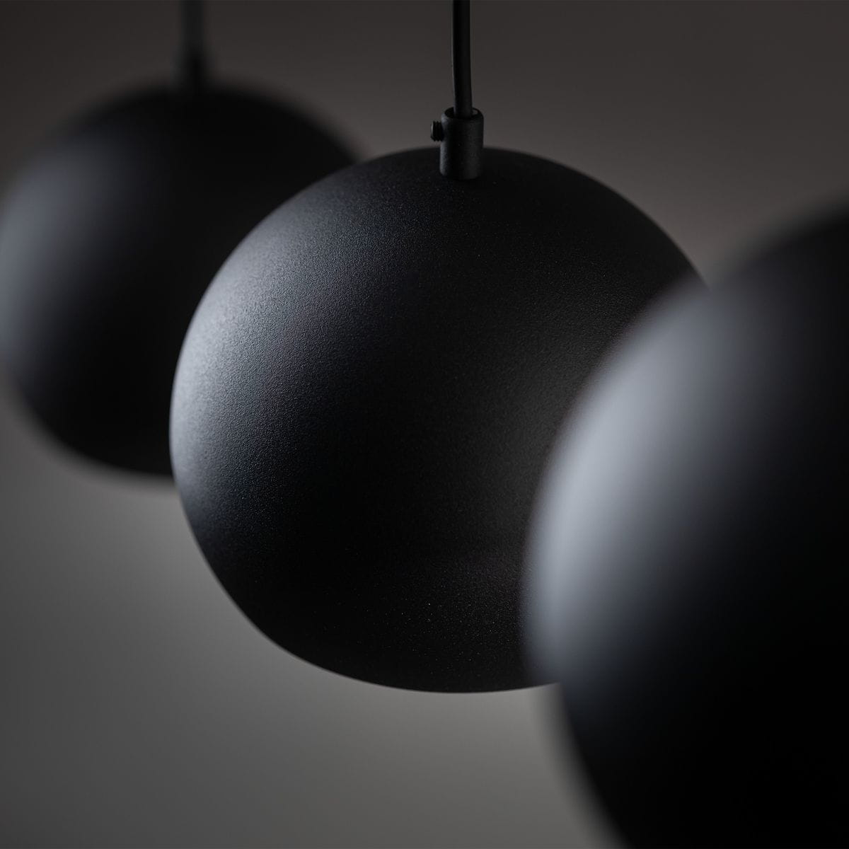 Czarna lampa wisząca Zoe z trzema okrągłymi kloszami E27, zawieszona na cienkich przewodach. Klosze mają matową powierzchnię, tworząc minimalistyczny design, idealny do nowoczesnych wnętrz. Ujęcie zbliżeniowe na detale kloszy.