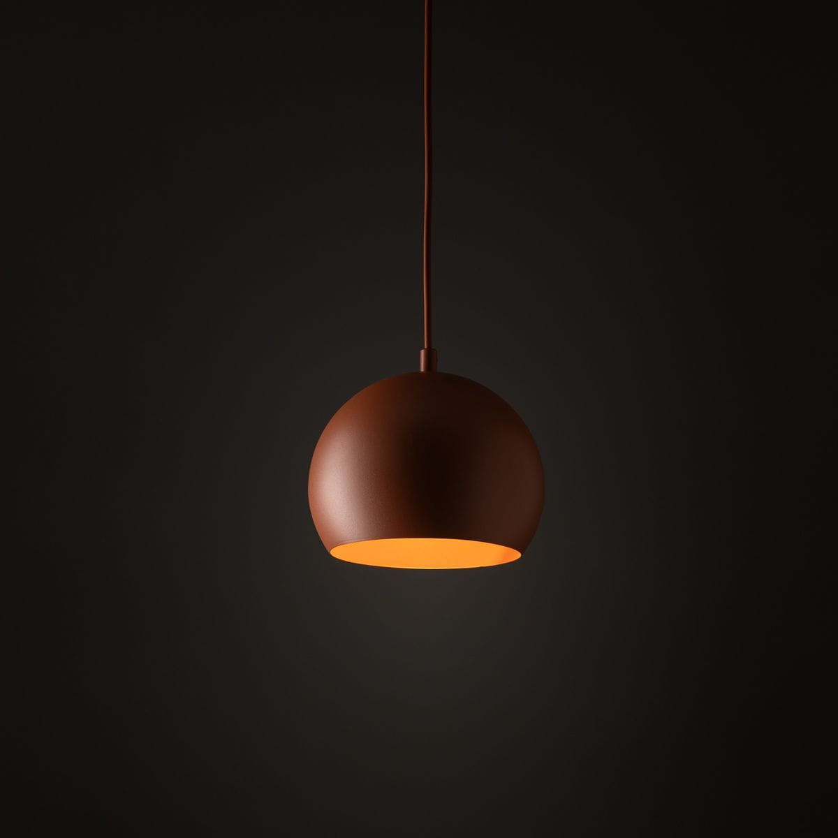 Ceglasta lampa wisząca Zoe D17, o okrągłym kształcie, zawieszona na cienkim przewodzie. Wnętrze klosza w kolorze żółtym, matowe wykończenie na zewnątrz. Prosta forma, odpowiednia do nowoczesnych wnętrz. Tło ciemne, minimalistyczne.