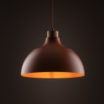 Lampa wisząca Cap o ceglastej barwie, z metalowym kloszem w kształcie dzwonu i drewnianym mocowaniem. Zawieszona na cienkim przewodzie, emituje ciepłe światło. Widok z dołu, na jednolitym ciemnym tle.