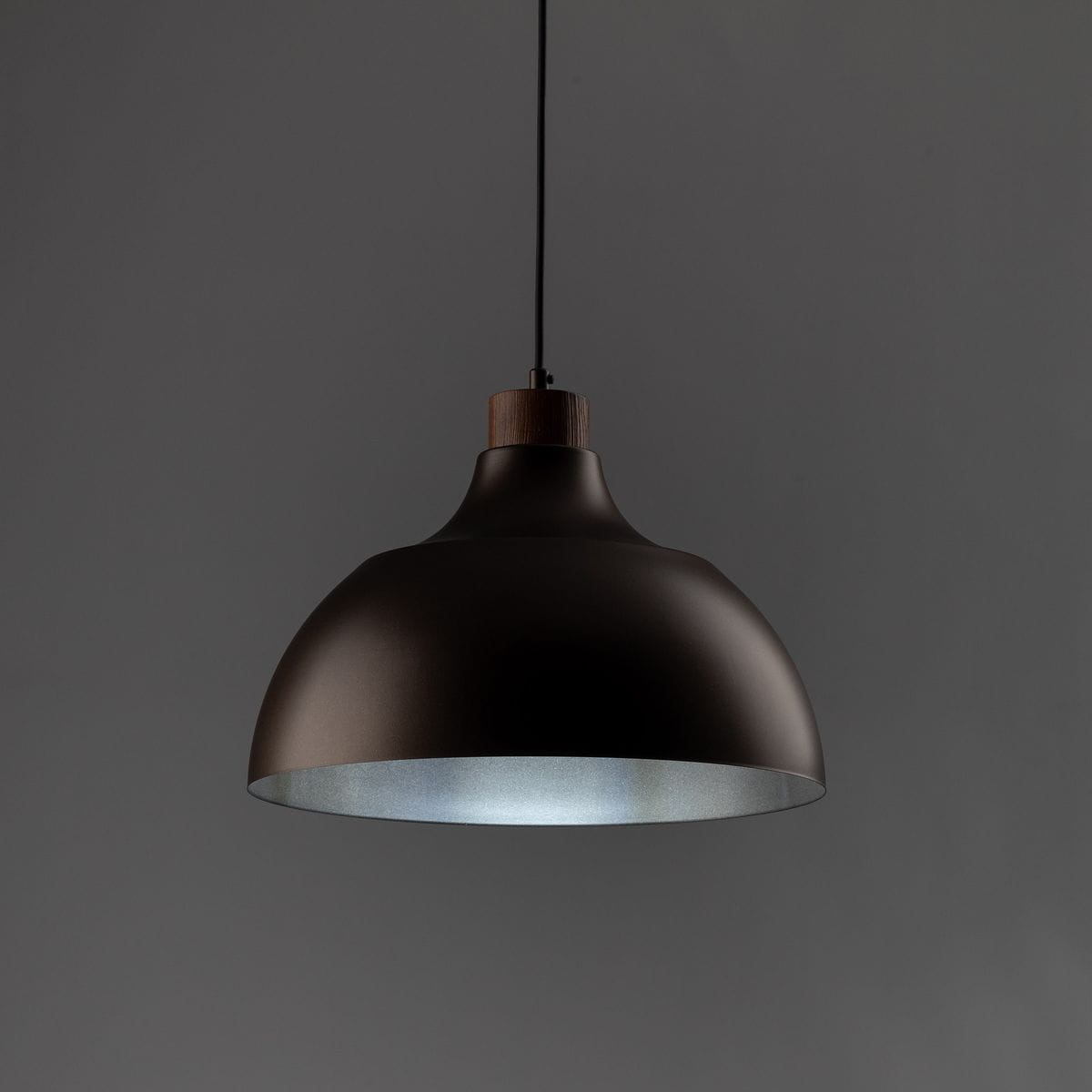 Lampa wisząca Cap 1xE27 w kolorze brązowym, z metalowym kloszem o zaokrąglonym kształcie i drewnianym elementem u góry. Zawieszona na cienkim przewodzie, idealna do nowoczesnych wnętrz. Tło w odcieniu szarości.