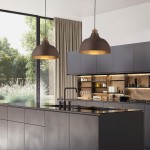 Brązowa lampa wisząca Cap z jedną oprawą E27, o zaokrąglonym kształcie, zawieszona nad nowoczesną kuchnią. Widoczne eleganckie wykończenie oraz ciepłe światło wewnętrzne. Tło z szarymi meblami i dużymi oknami, wprowadzającymi naturalne światło.