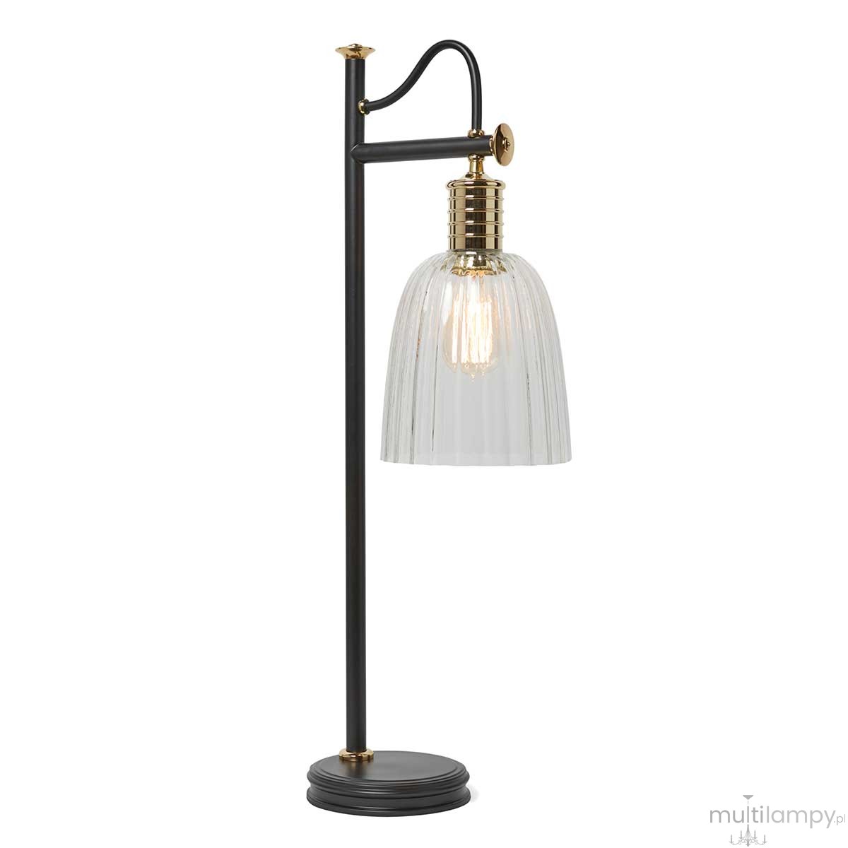 Lampka stołowa Douille z metalowym, czarnym stelażem i przezroczystym, szklanym kloszem w kształcie dzwonu. Uchwyt w kolorze złotym. Lampa ma miejsce na żarówkę E27. Ujęcie z boku, prezentujące całość oraz detal klosza.