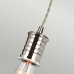 Lampa wisząca z oprawą w polerowanym niklu, wykończona w formie cylindrycznej z rowkami. Zawieszona na sznurze tekstylnym w jasnym kolorze. Widoczna gniazdówka E27 dla żarówki, z przezroczystą żarówką.