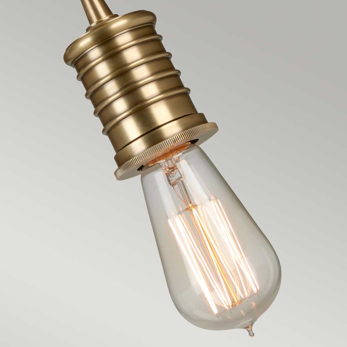 Lampa wisząca z postarzanym mosiądzu, z gniazdem E27. Ujęcie z góry, ukazujące dekoracyjny klosz w kształcie kropli oraz detalowane wykończenie górnej części. Klosz przezroczysty, z widocznymi żarówkami. Tło jasne, neutralne.