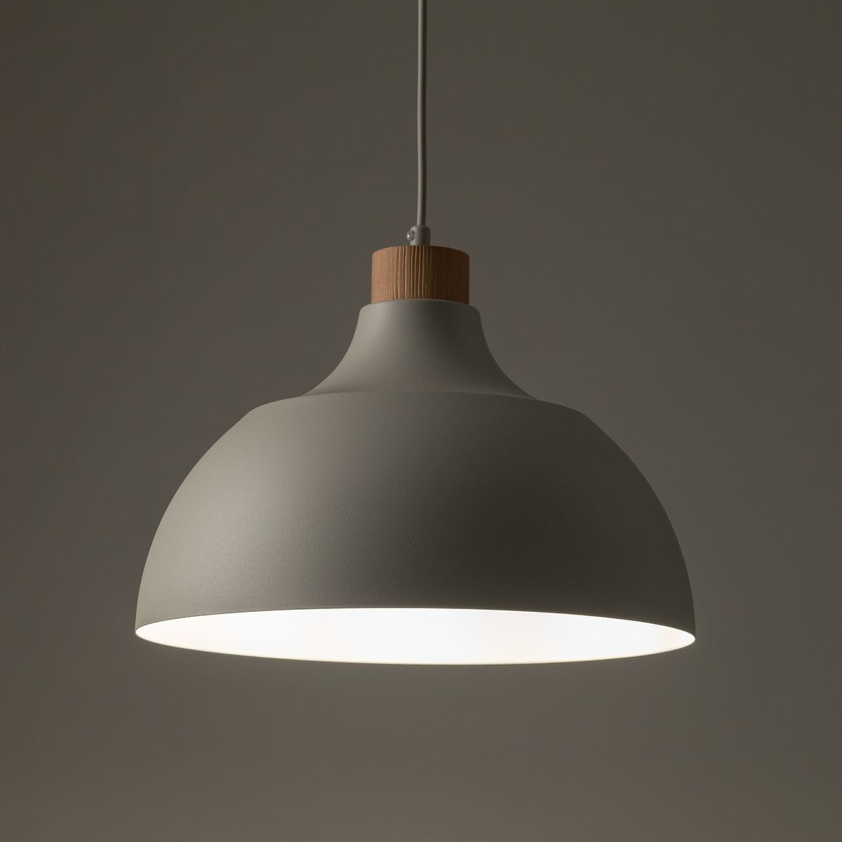 Beżowa lampa wisząca Cap z oprawą w kształcie półkuli, wykonana z matowego materiału, z drewnianym detalem u góry. Zawieszona na cienkim przewodzie, emituje światło z dolnej krawędzi, idealna do nowoczesnych wnętrz.