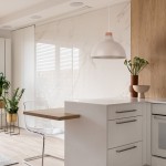 Beżowa lampa wisząca z kloszem w kształcie miski, zawieszona na cienkim przewodzie. Widoczna w nowoczesnej kuchni z białymi meblami, drewnianymi akcentami i roślinami w tle. Idealna do oświetlenia przestrzeni roboczej.
