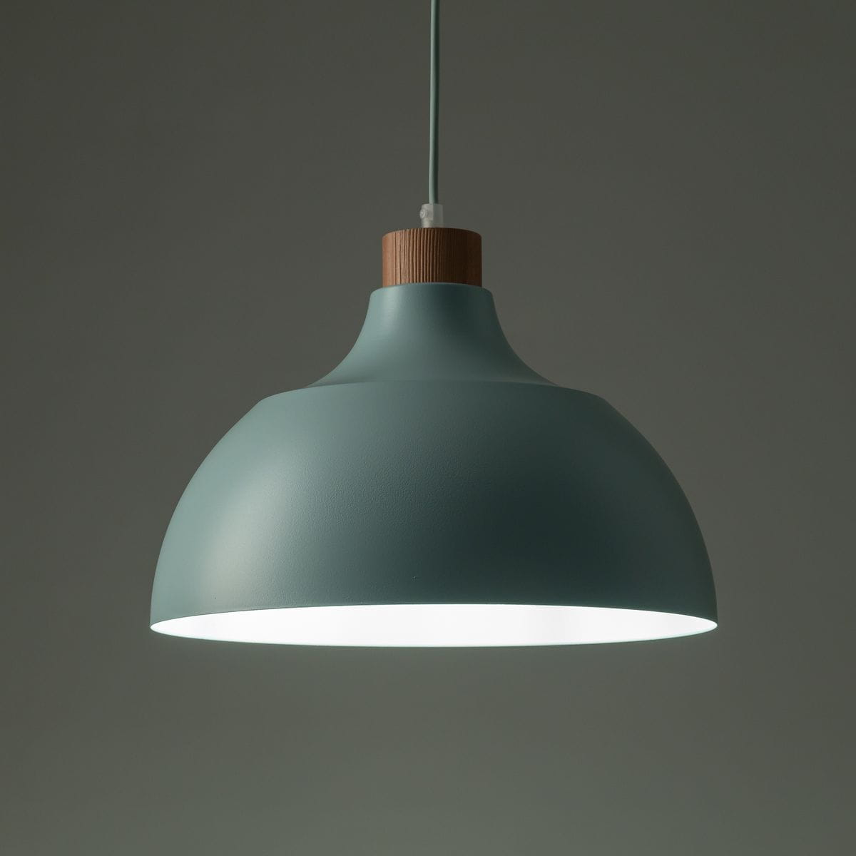 Lampa wisząca w kolorze miętowym z kloszem w kształcie półkuli, z drewnianym elementem u góry. Zawieszona na cienkim przewodzie, idealna do oświetlenia wnętrz.