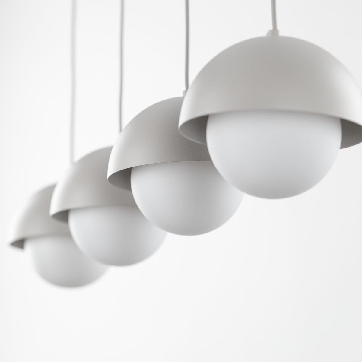 Beżowa lampa wisząca Bono z czterema kloszami w kształcie półkul, wykonana z matowego materiału, zawieszona na białych linkach. Klosze mają białe, okrągłe żarówki G9, tworząc nowoczesny i minimalistyczny design na jasnym tle.