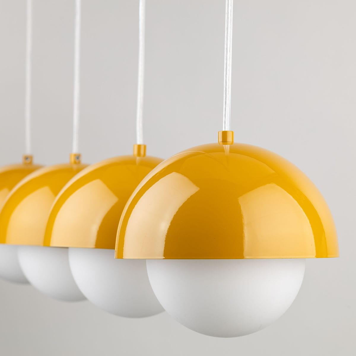 Lampa wisząca Bono z czterema kloszami w kolorze żółtym i białym. Klosze mają kształt półkulisty, z gładką, błyszczącą powierzchnią, zawieszone na białych linkach. Produkt idealny do nowoczesnych wnętrz.