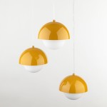 Lampa wisząca Bono z trzema kloszami w kształcie półkul, w kolorze ochry i białym. Klosze zawieszone na cienkich, białych przewodach, umieszczone w równych odstępach. Tło jednolite, jasne.