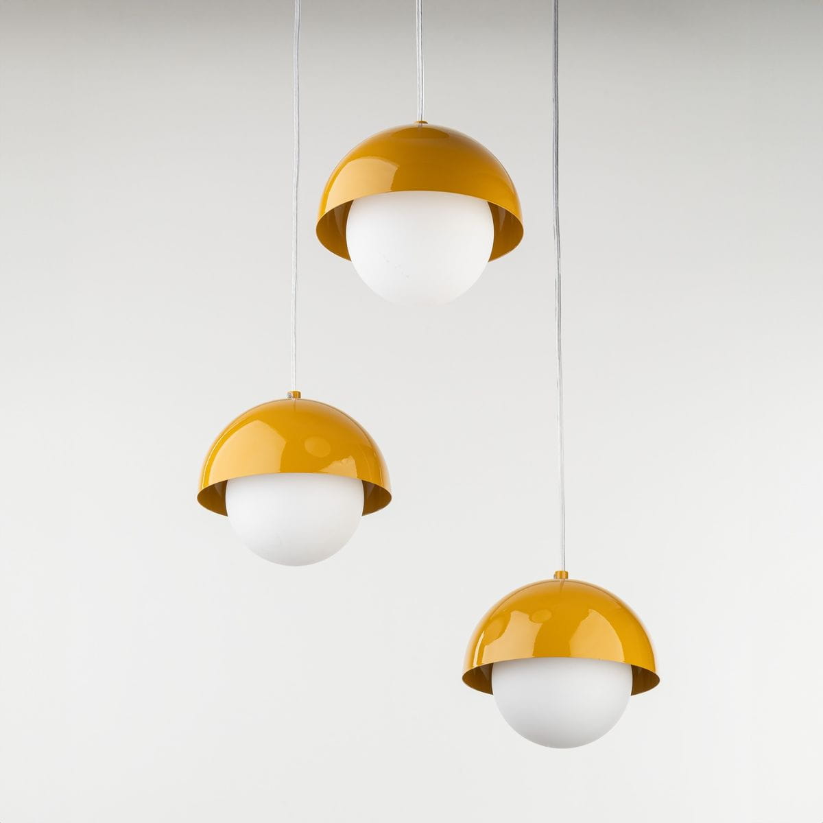 Lampa wisząca Bono z trzema źródłami światła G9, z kloszami w kształcie półkul, w kolorze białym z żółtymi, błyszczącymi osłonami. Produkt zawieszony na białych kablach, prezentowany na jasnym tle.