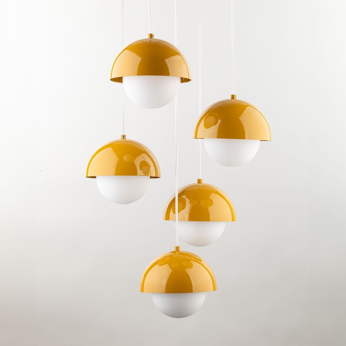 Lampa wisząca Bono z pięcioma źródłami światła G9, w kolorze żółtym i białym. Posiada półkuliste klosze z błyszczącego metalu oraz matowego szkła. Zawieszona na białych przewodach, prezentuje nowoczesny design.