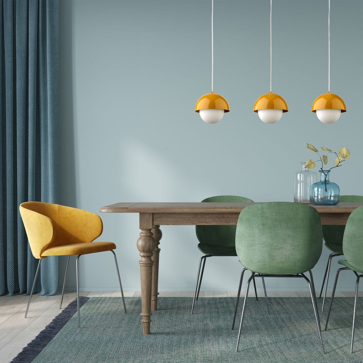 Lampa wisząca Bono D17 z jednym źródłem światła G9, w kolorze ochry, z zaokrąglonym kloszem połączonym z białą kulą. Zawieszona nad drewnianym stołem, w otoczeniu zielonych krzeseł i żółtego fotela. Tło w pastelowym odcieniu niebieskiego.