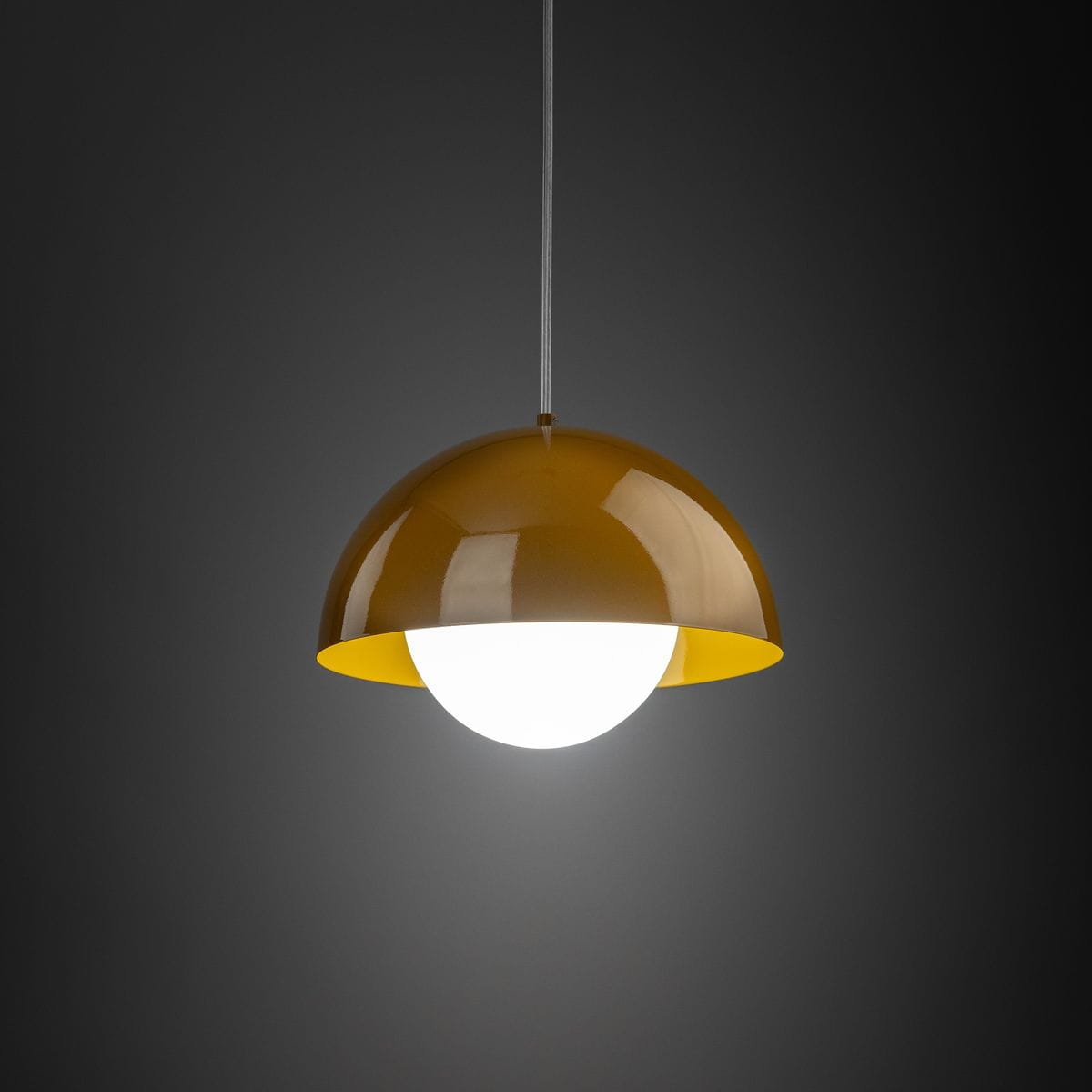 Lampa wisząca Bono D27 w kolorze ochry z połyskującym kloszem w kształcie półkuli, z białą żarówką G9. Zawieszona na cienkim przewodzie na ciemnym tle, prezentuje nowoczesny design.