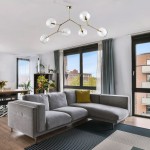 Lampa sufitowa Fairy w kolorze złotym i transparentnym, z sześcioma kulistymi kloszami na ramionach. Zamontowana na suficie, w nowoczesnym wnętrzu z szaro-białymi elementami. Widoczna w aranżacji z kanapą i oknami.