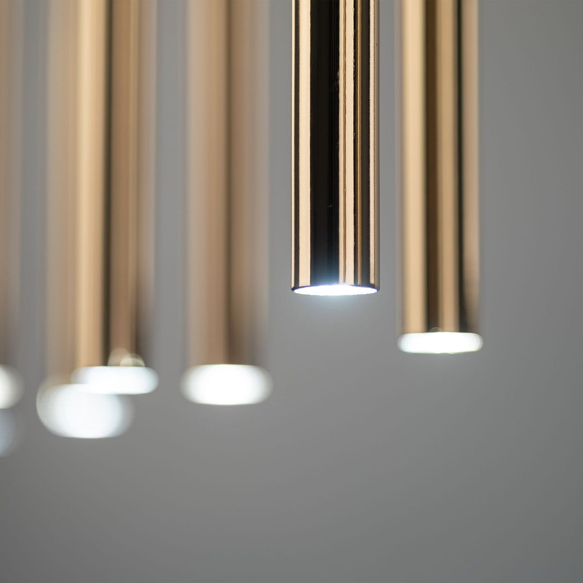 Lampa wisząca Piano z 12 źródłami światła G9, w kolorze czarnym i złotym. Widoczne metalowe rurki o błyszczącej powierzchni, emitujące jasne światło. Ujęcie z bliska, pokazujące detale konstrukcji i efekt oświetlenia.