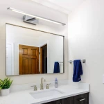 Kinkiet LED Isla IP44 w kolorze chromu, o długości 62 cm i mocy 20W, zamontowany nad lustrem w łazience. Prosty, prostokątny kształt z białym światłem, umieszczony na jasnej ścianie, w otoczeniu umywalki i akcesoriów łazienkowych.