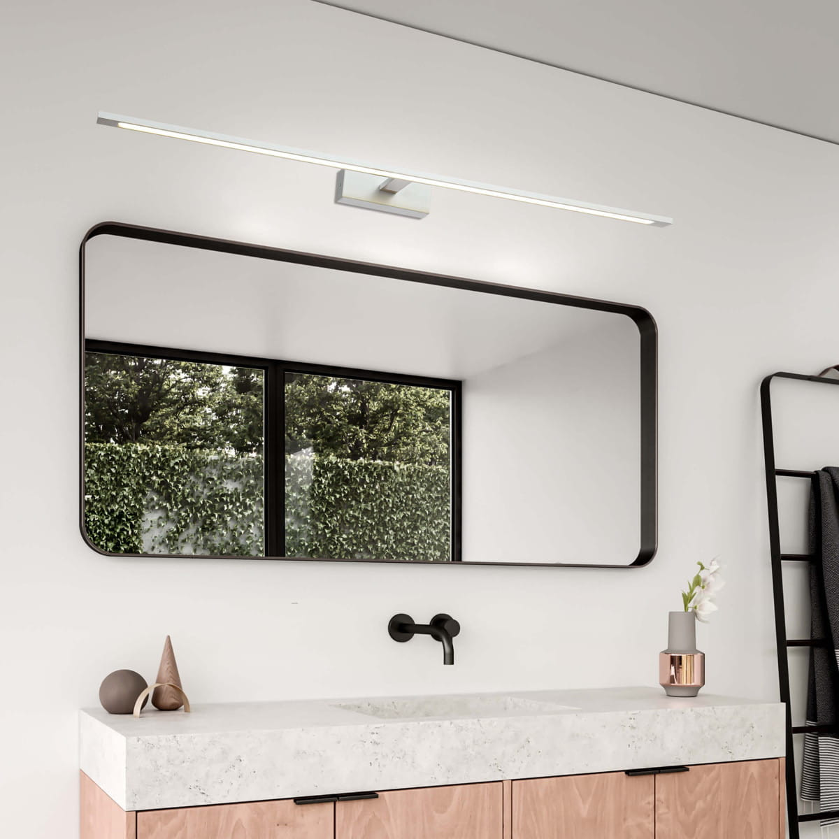 Kinkiet LED Isla IP44 w chromowanej obudowie, długość 96 cm, zamontowany nad dużym lustrem. Oświetlenie w neutralnym kolorze, na tle nowoczesnej łazienki z drewnianą szafką i oknem wypełnionym zielenią.