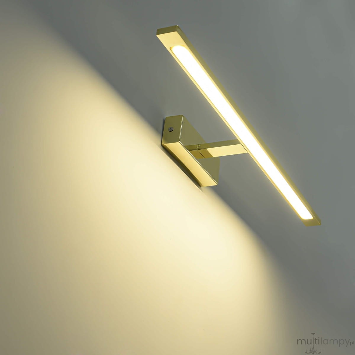 Kinkiet LED Isla IP44 w kolorze złotym, o długości 62 cm i mocy 20 W. Posiada prostokątną, smukłą formę z zamontowanym źródłem światła, skierowany ku górze, na jasnym tle. Idealny do nowoczesnych wnętrz.