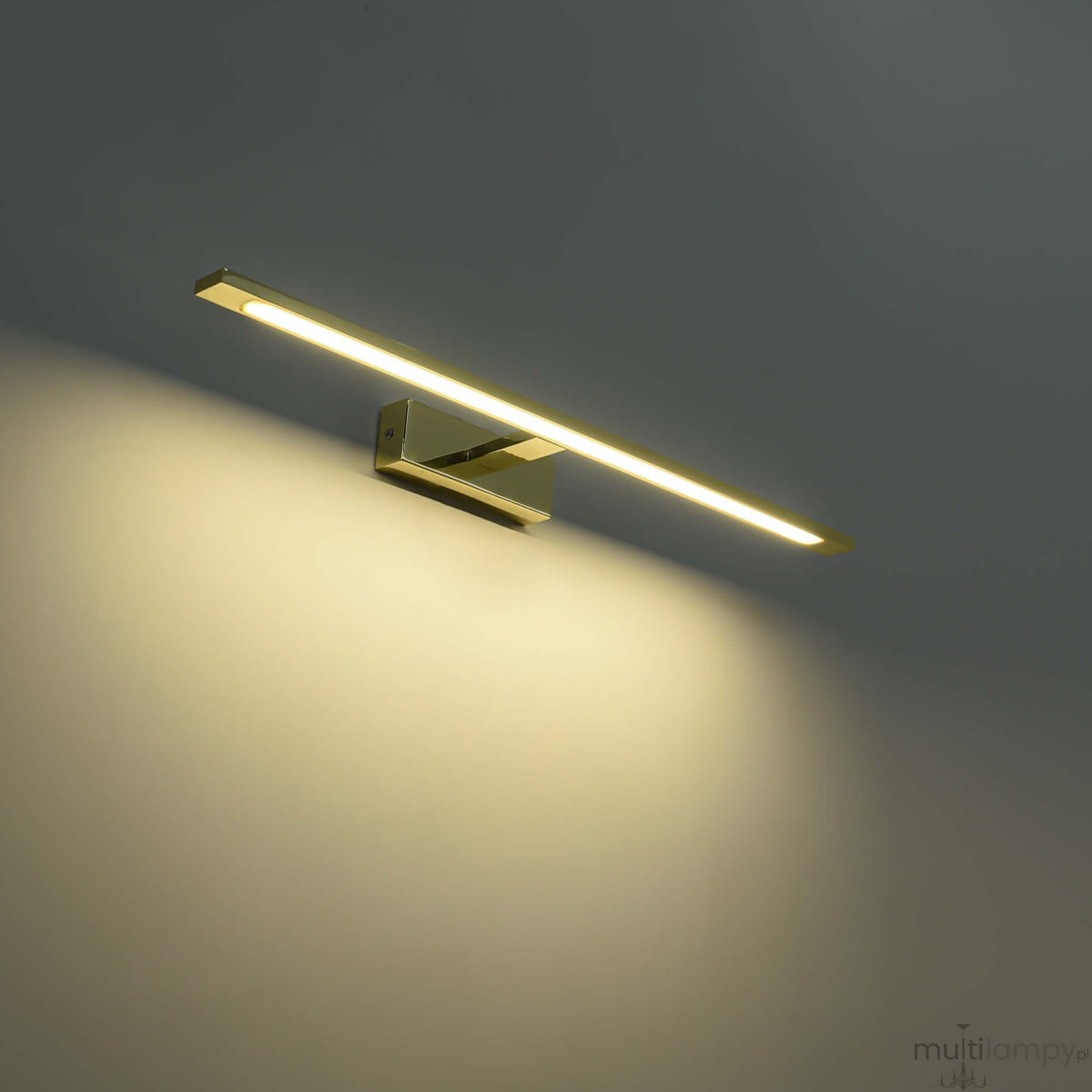 Kinkiet LED Isla IP44 w kolorze złotym, prostokątny, montowany na ścianie. Emituje ciepłe światło, złożony z cienkiego panelu i metalowej podstawy. Ujęcie frontalne, na jednolitym tle, podkreślające minimalistyczny design.