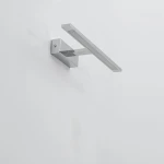 Kinkiet LED Isla IP44 w kolorze chromu, z prostokątną, płaską oprawą. Zainstalowany na ścianie w pozycji poziomej. Wykończenie błyszczące, minimalistyczny design, idealny do nowoczesnych wnętrz. Tło jasne, neutralne.