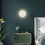 Kinkiet Luna 2xG9 w kolorze białym, okrągły, zamontowany na ciemnej ścianie. W tle widoczna komoda w zielonym kolorze, z dekoracjami i rośliną. Oświetlenie tworzy ciepłą atmosferę w aranżacji sypialni.