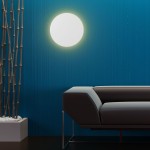 Kinkiet Luna 4xG9 w kolorze białym, okrągły, zamontowany na niebieskiej ścianie. W tle widoczna ciemnoszara sofa i ozdobne pędy roślin w jasnym doniczce. Oświetlenie emituje miękkie, ciepłe światło, tworząc przytulną atmosferę.