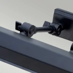 Kinkiet obrazowy Chawton M w kolorze czarnym, z dwoma miejscami na żarówki E14. Zbliżenie na mechanizm mocujący i regulacyjny, z metalowymi elementami i prostą, matową fakturą. Ujęcie pod kątem, ukazujące detale konstrukcji.