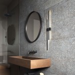 Kinkiet Flash w kolorze czarnym, z dwoma źródłami LED o mocy 24W, zamontowany na ścianie w łazience, obok okrągłego lustra. Oświetlenie emitujące łagodne światło, w nowoczesnym, minimalistycznym stylu.