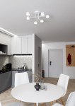 Biała lampa sufitowa Halo z sześcioma źródłami światła GX53, zamontowana na suficie w kuchni. Ma minimalistyczny design, z ramieniem rozłożonym w formie gwiazdy, pasujący do jasnych wnętrz. Tło to przestrzeń z szarymi meblami i stołem.