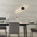 Kinkiet Java 2xLED/30W w kolorze czarnym, zamontowany na ścianie, z okrągłym elementem oraz dwoma poziomymi paskami światła. W tle stół z szarymi krzesłami, szklankami oraz naczyniami na jasnym tle.