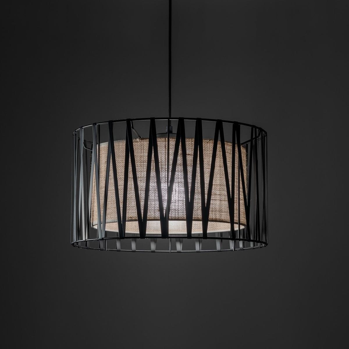 Lampa wisząca Harmony z oprawą w kolorze czarnym i brązowym, o okrągłym kształcie. Metalowy klosz z geometrycznym wzorem, odsłaniający wewnętrzny materiał w odcieniu brązowym. Zawieszona na cienkim przewodzie, na ciemnym tle.