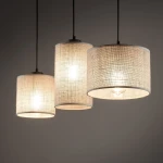 Lampa wisząca Juta z trzema abażurami w kolorze naturalnym z juty, zawieszona na czarnych kablach. Abażury mają okrągły kształt, a każdy z nich jest podświetlony, tworząc ciepłe światło. Tło ciemnoszare, minimalistyczne.