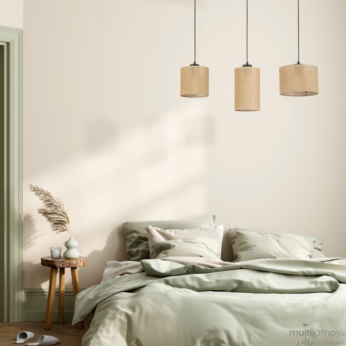 Lampa wisząca Juta z trzema kloszami w kolorze czarnym i brązowym, zawieszona nad łóżkiem, w otoczeniu pastelowych poduszek i narzuty. Klosze wykonane z materiału, w kształcie cylindrów, na czarnych przewodach.