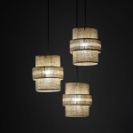 Lampa wisząca Calisto w kolorze czarnym i brązowym, z trzema kloszami w formie cylindrów, wykonana z teksturowanego materiału. Zawieszona na cienkich linach, emitująca ciepłe światło, umieszczona na ciemnym tle.