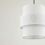 Lampa wisząca Calisto D20 w kolorze białym z czarnym zawieszeniem. Składa się z dwóch okrągłych kloszy z teksturowanego materiału, umieszczonych jeden na drugim, z widoczną oprawką na żarówkę E27.