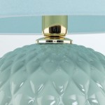 Lampa stołowa Santana z kloszem w kolorze miętowym, o fakturze przypominającej diamenty. Podstawa w złotym kolorze, z detalami metalowymi. Wymiary i inne szczegóły nie są widoczne.